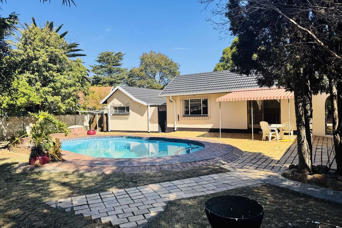 Rear exterior view featuring a swimming pool, paved patio area with an awning, and established garden surroundings.