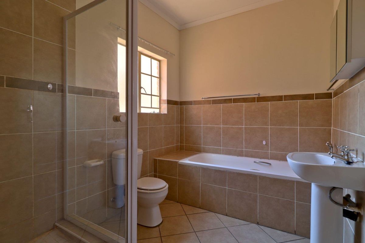 A functional bathroom featuring a pedestal basin, a built-in bathtub, and a separate glass-enclosed shower with neutral ceramic wall and floor tiles.