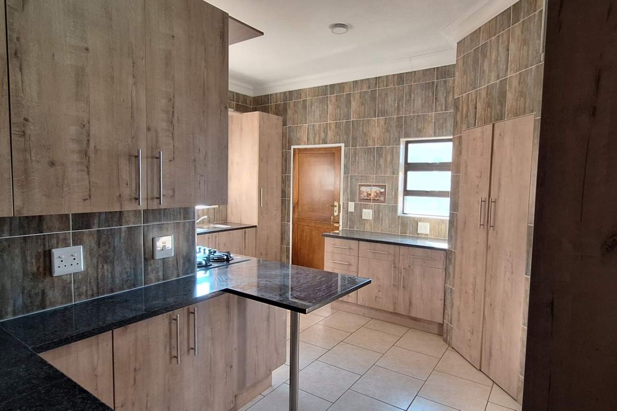 Modern kitchen featuring wood-look cabinetry, dark granite countertops, gas hob, and tiled finishes throughout, offering a clean and functional workspace.