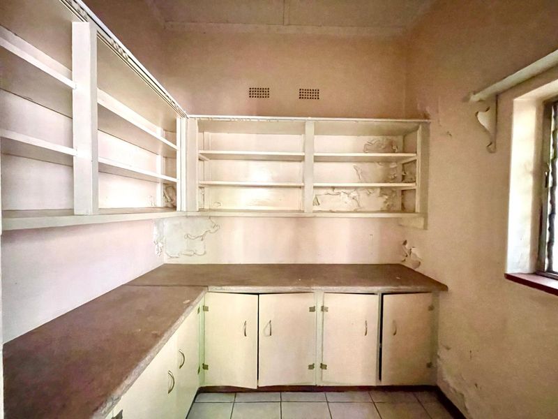 A dated scullery or pantry area featuring built-in cabinetry and open shelving, requiring significant cosmetic renovation and wall repairs.