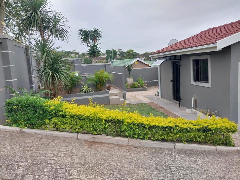 A well-maintained rear exterior view of the cottage featuring a paved walkway, landscaped garden beds, and secure boundary walls.