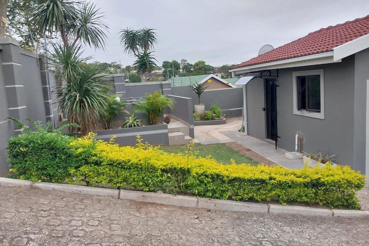 A well-maintained rear exterior view of the cottage featuring a paved walkway, landscaped garden beds, and secure boundary walls.
