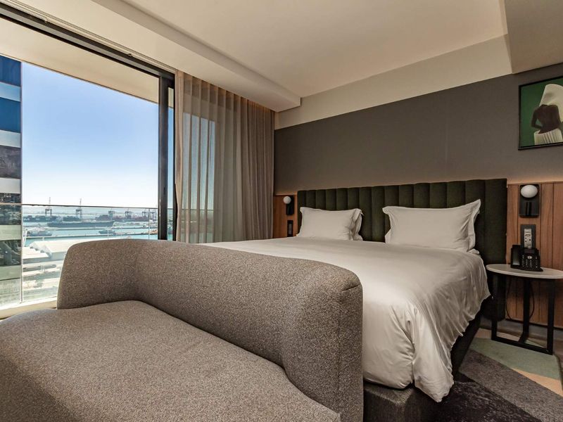 Modern bedroom featuring a built-in upholstered headboard, integrated bedside lighting, and large sliding glass doors opening to a balcony with harbor views.