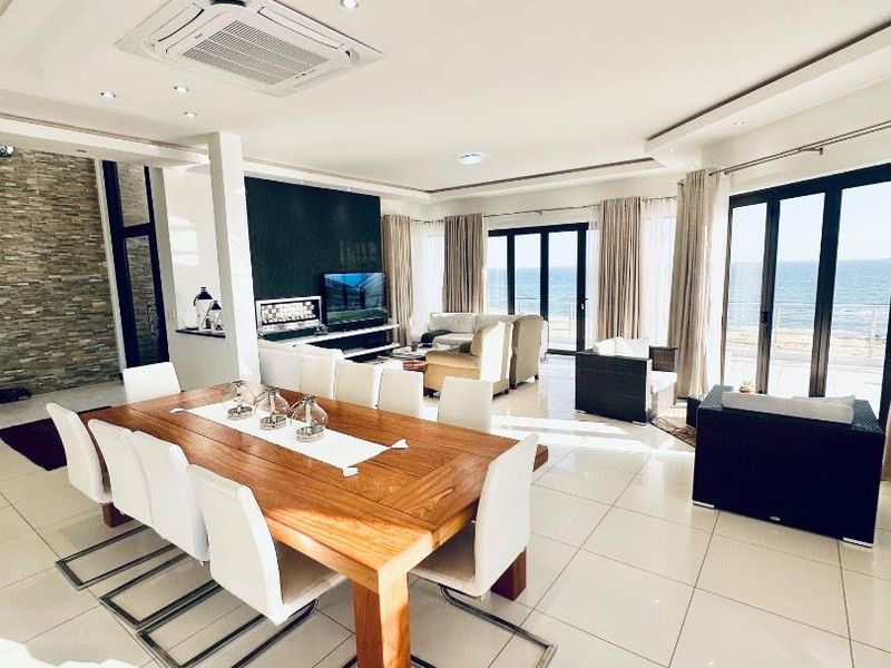 Spacious open-plan living and dining area featuring high-gloss tiled floors, recessed ceiling with ducted air conditioning, and expansive sliding doors with ocean views.