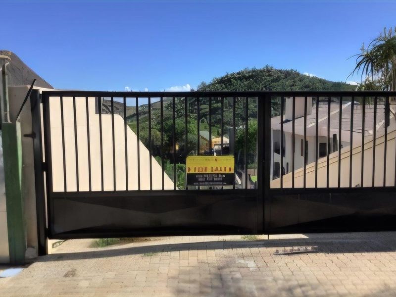 A view of the property entrance featuring a black metal security gate and paved driveway area.