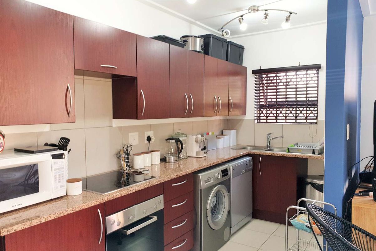 A functional kitchen featuring dark wood cabinetry, granite countertops, a built-in oven, hob, and integrated space for laundry and dishwashing appliances.