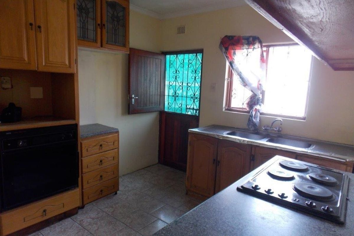 A functional kitchen featuring wooden cabinetry, laminate countertops, a built-in oven, hob, and double basin sink, with direct access to the exterior.