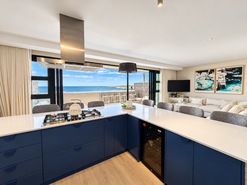 Modern open-plan kitchen featuring a large island with gas cooktop, integrated wine cooler, and seamless flow to a balcony with ocean views.