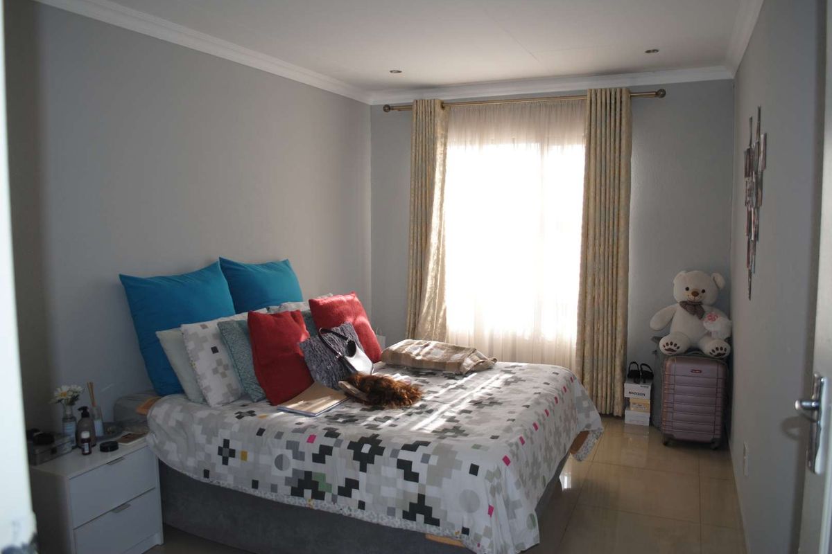 A well-lit bedroom featuring neutral wall tones, tiled flooring, and a large window with fitted curtain tracks.