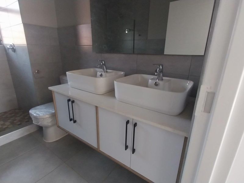 Modern bathroom featuring a double vanity with vessel sinks, contemporary mixer taps, a large wall-mounted mirror, and a spacious walk-in shower.