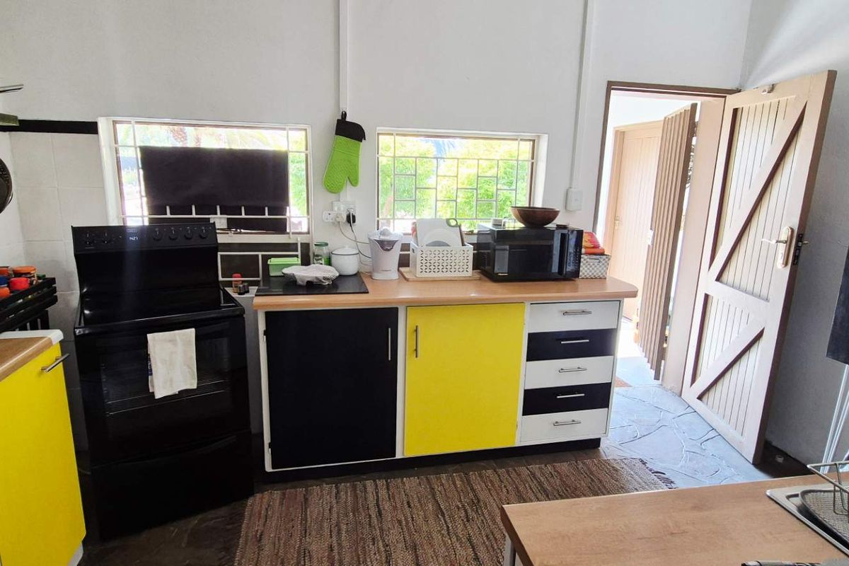 A functional kitchen featuring a freestanding stove, contrasting yellow and black cabinetry, wooden countertops, and direct access to an adjacent room.