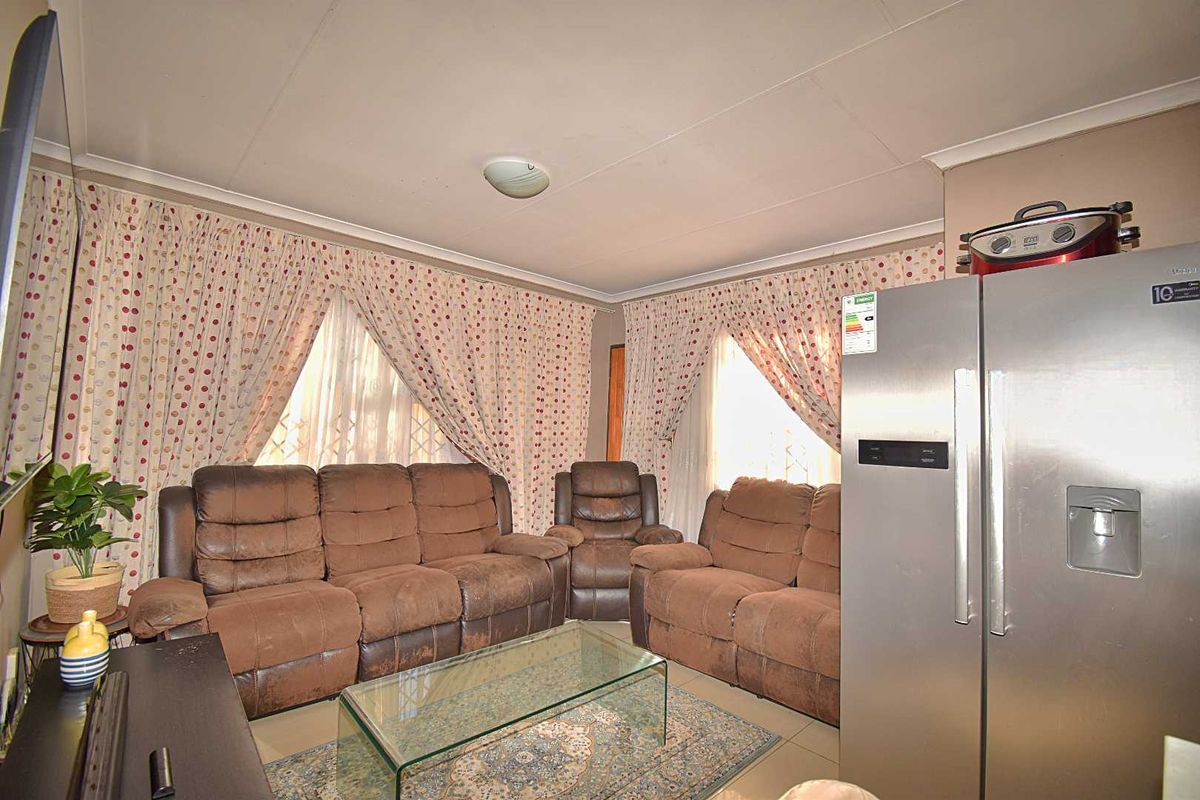A living area featuring tiled flooring and large windows with curtains, providing a functional space for relaxation.