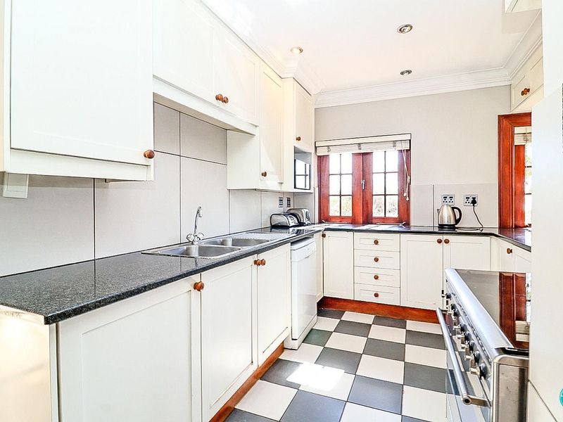 A well-maintained kitchen featuring white cabinetry, granite countertops, a gas stove, and classic black and white checkered floor tiles.