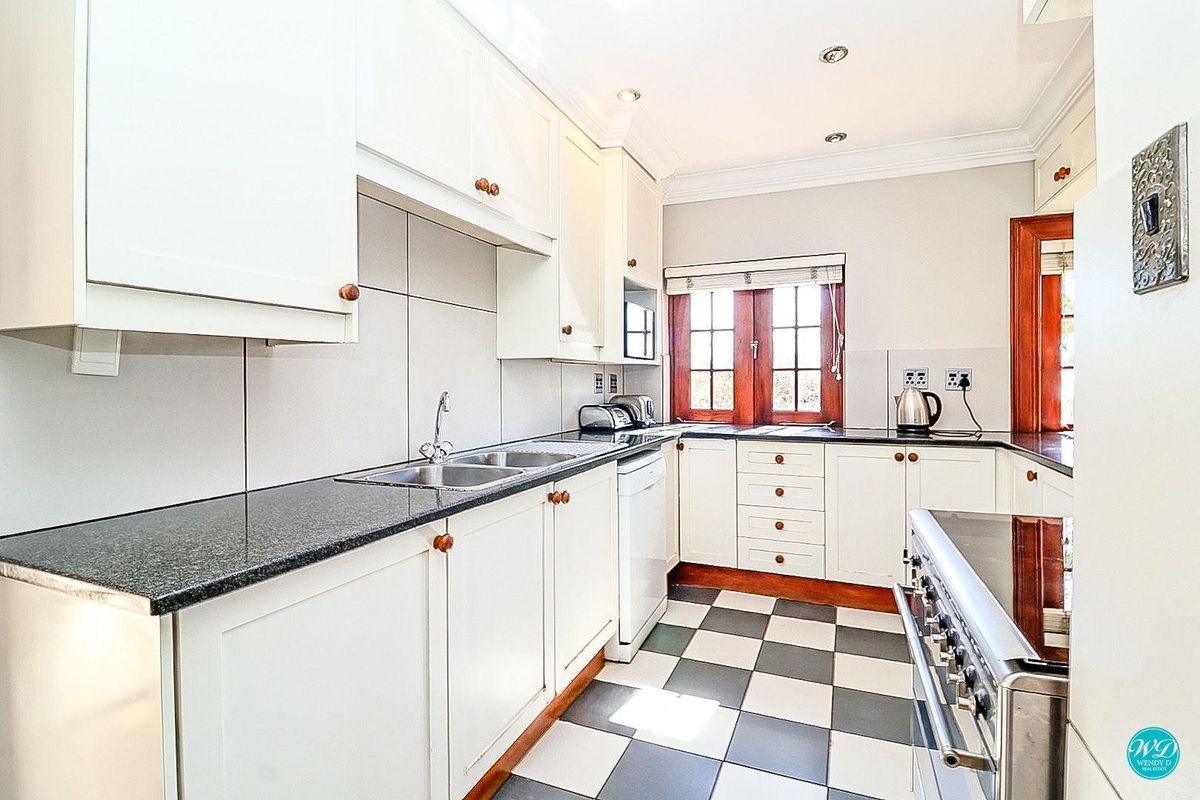 A well-maintained kitchen featuring white cabinetry, granite countertops, a gas stove, and classic black and white checkered floor tiles.