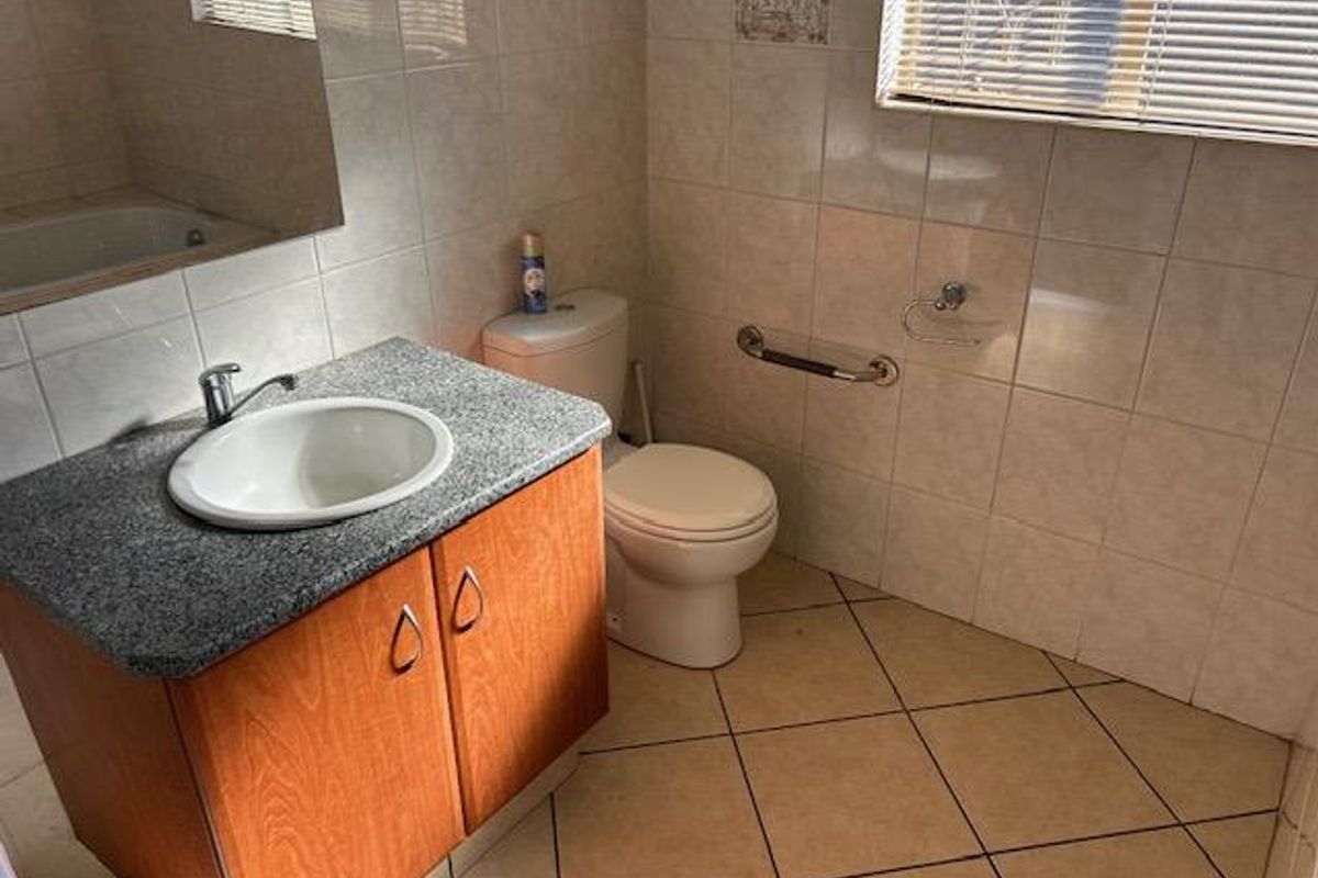 A functional bathroom featuring a vanity cabinet with a granite countertop, a drop-in sink, a toilet, and wall-mounted grab rails.