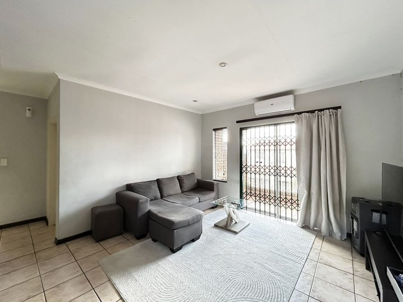 A living room featuring tiled flooring, a split-system air conditioner, and a sliding glass door with a security gate leading to the exterior.