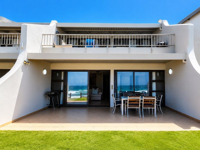 A spacious ground-floor tiled patio featuring sliding glass doors, leading to a well-maintained lawn with an upper balcony above.