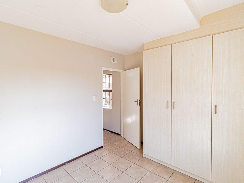 A clean, empty bedroom featuring neutral tiled flooring and ample built-in cupboard storage, offering a versatile space ready for personalization.