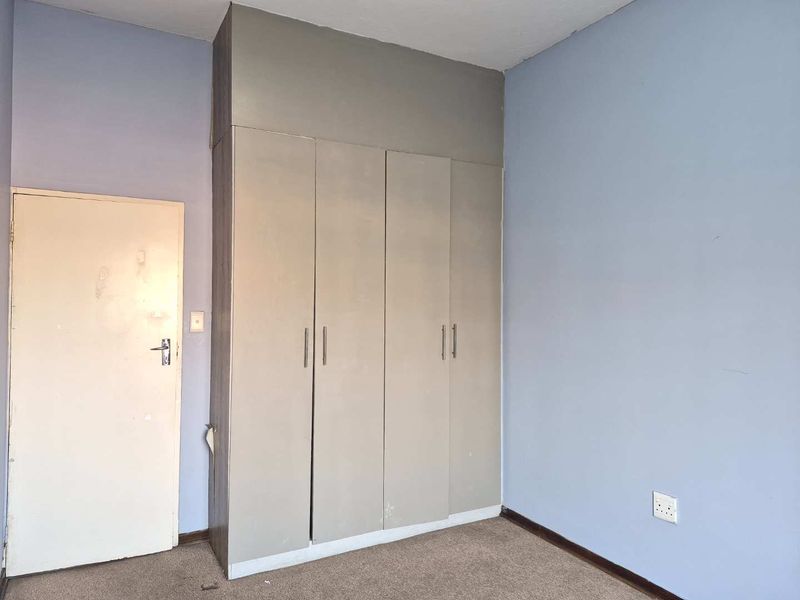 A vacant bedroom featuring built-in cupboards, carpeted flooring, and light blue walls, offering a blank canvas for potential updates and personalization.