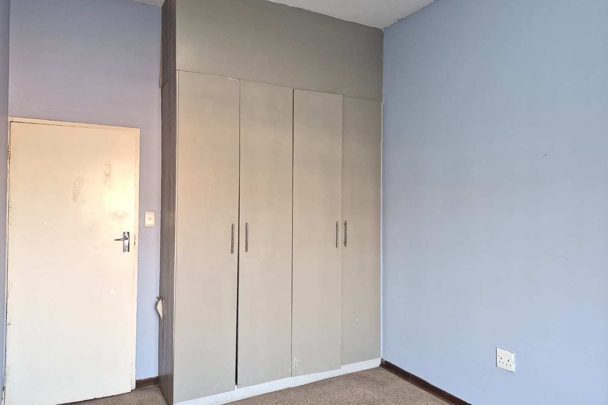 A vacant bedroom featuring built-in cupboards, carpeted flooring, and light blue walls, offering a blank canvas for potential updates and personalization.