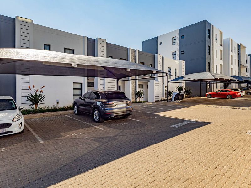 Modern apartment complex exterior featuring paved parking bays with shade cloth carports and contemporary building architecture.