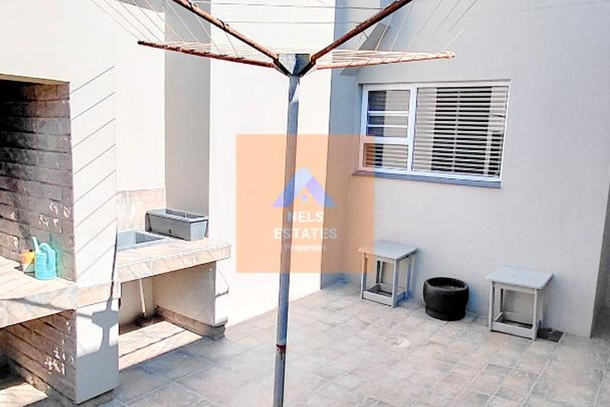 Rear courtyard area featuring a built-in braai, tiled flooring, and a rotary clothesline, providing a functional outdoor space.