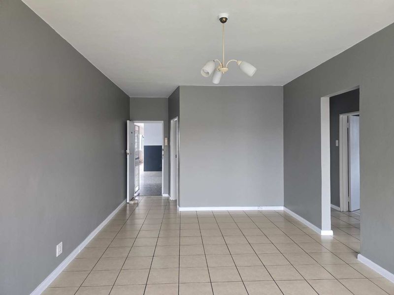 A spacious, empty living area featuring neutral grey walls, ceramic tiled flooring, and a central ceiling light fixture.