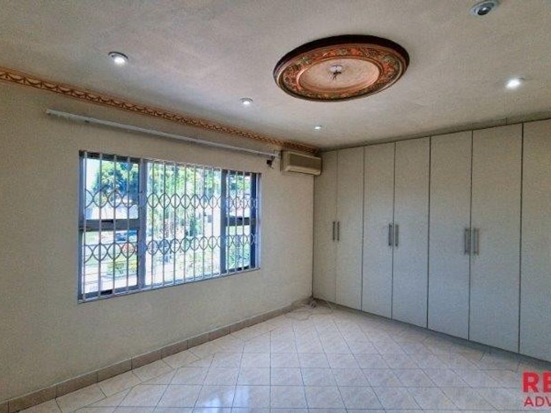 Spacious bedroom featuring extensive built-in cupboards, tiled flooring, decorative ceiling rose, and a wall-mounted air conditioning unit.