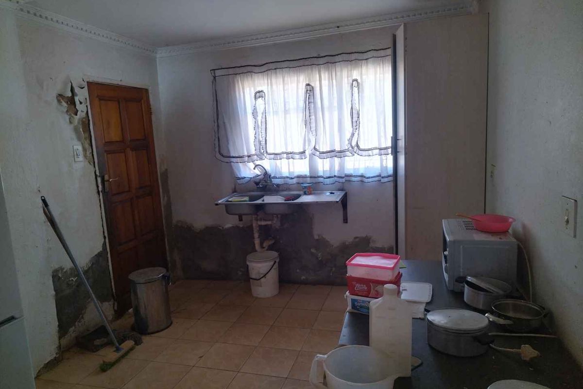 A kitchen space requiring significant renovation, featuring a double basin sink, tiled flooring, and visible wall damage needing repair.