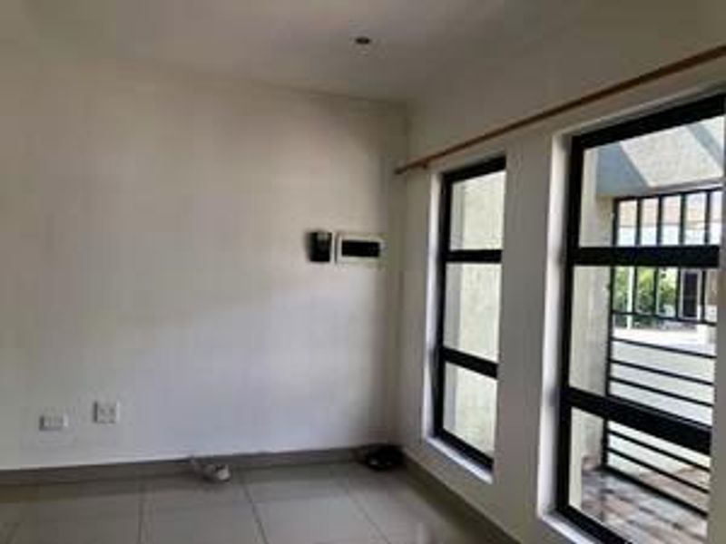 An empty living area featuring tiled flooring, large windows for natural light, and an integrated security gate leading to the exterior.
