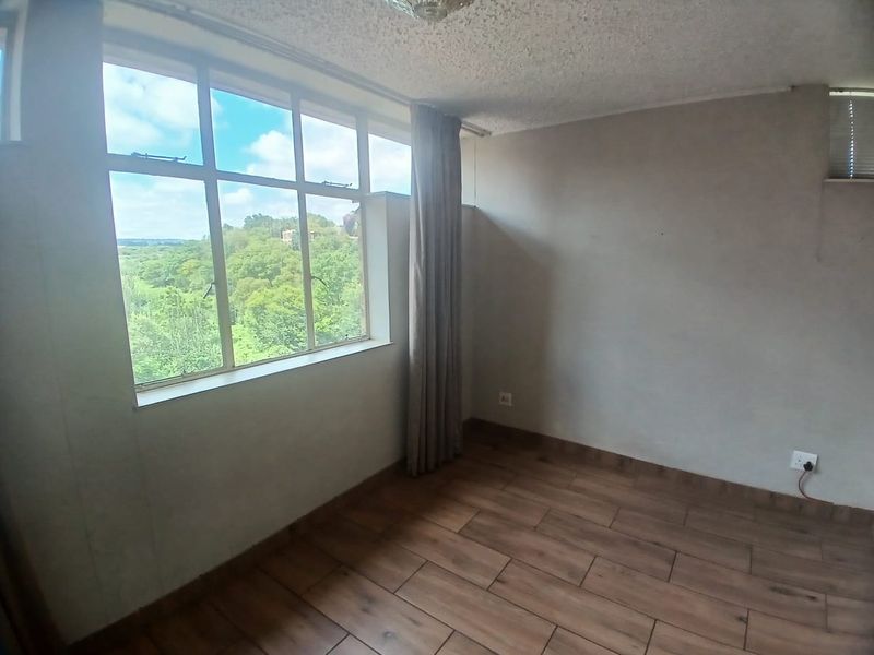 An empty bedroom featuring wood-look tile flooring, a textured ceiling, and a large window providing natural light and scenic views.
