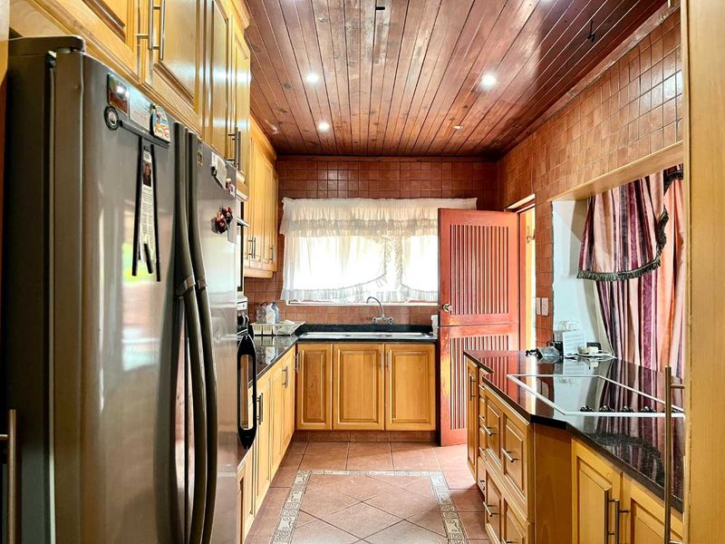 A traditional kitchen featuring wooden cabinetry, granite countertops, tiled backsplash, and a warm wooden tongue and groove ceiling with recessed lighting.