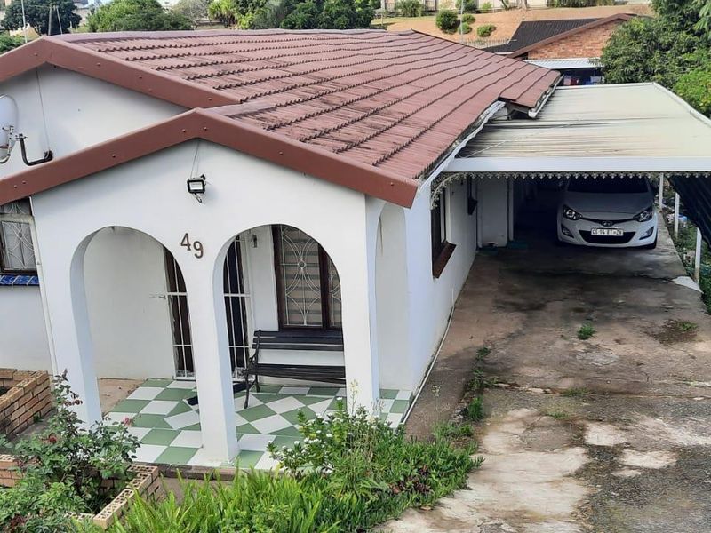 Front elevation of a single-story house featuring an arched entrance porch, tiled roof, and an attached covered carport with a concrete driveway.