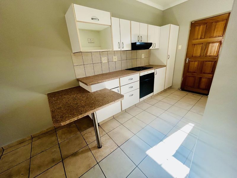 A functional kitchen featuring built-in cabinetry, a hob, an oven, and an extractor fan, with tiled flooring and a breakfast counter.