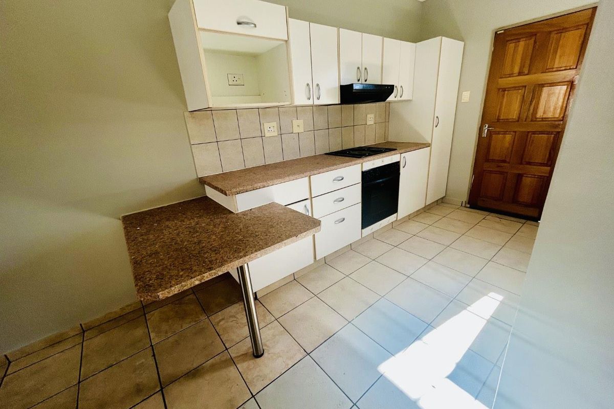 A functional kitchen featuring built-in cabinetry, a hob, an oven, and an extractor fan, with tiled flooring and a breakfast counter.