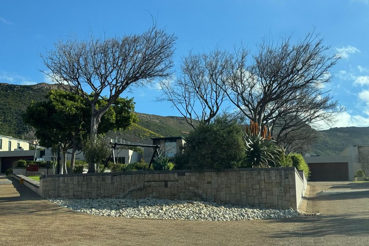 Front view of the property featuring a stone-clad retaining wall, paved driveway, and established garden landscaping against a mountain backdrop.