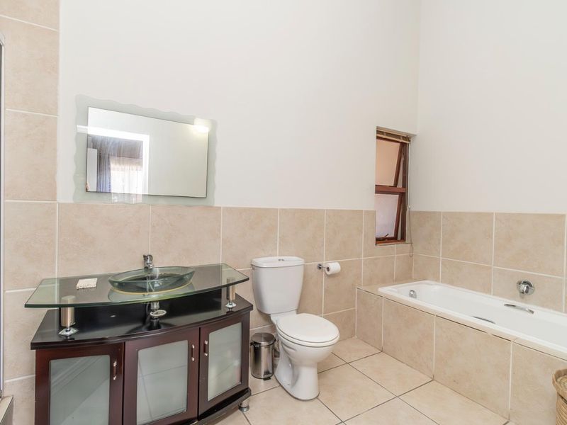 A functional bathroom featuring a glass vessel sink vanity, a built-in bathtub, a toilet, and neutral wall and floor tiling.