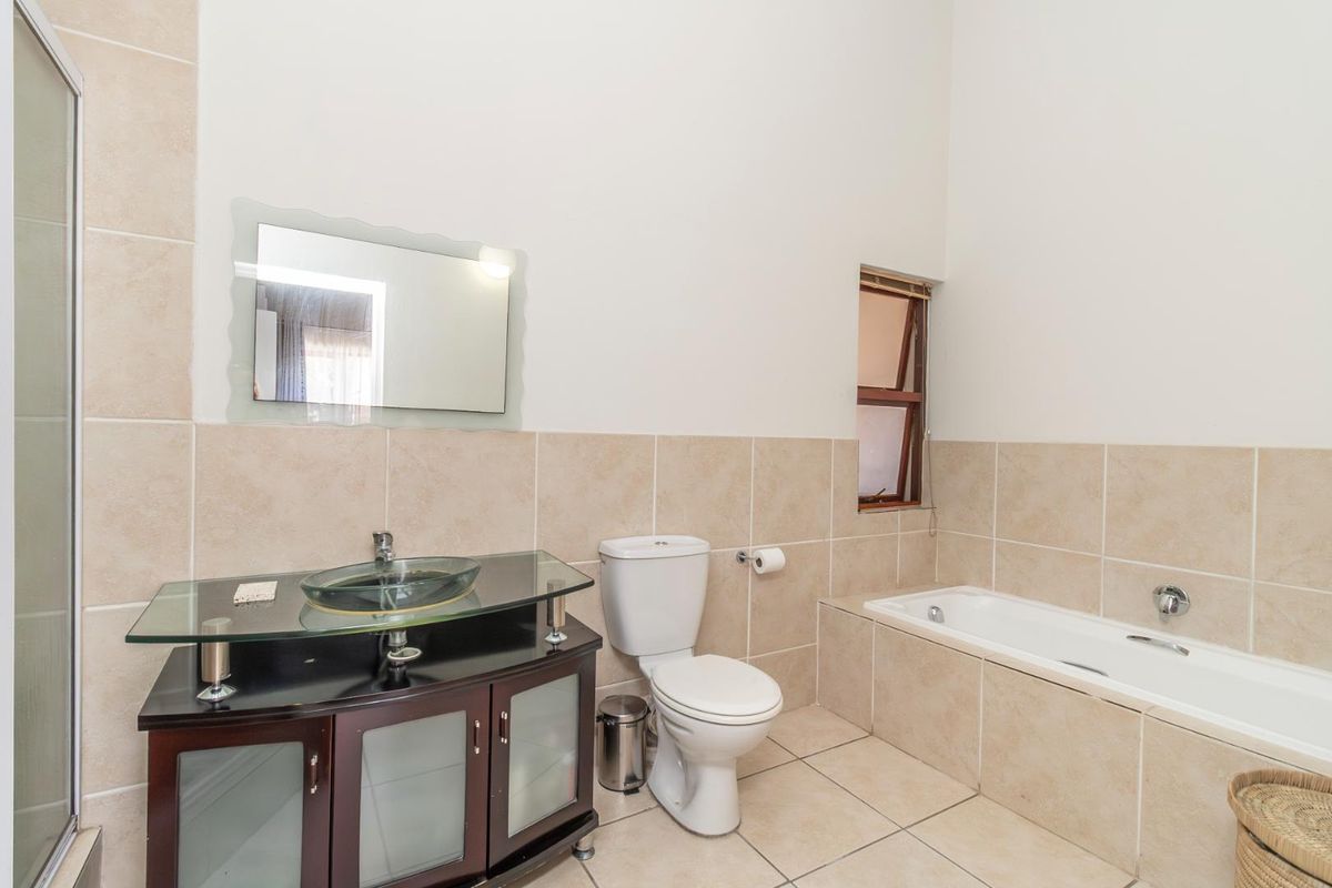 A functional bathroom featuring a glass vessel sink vanity, a built-in bathtub, a toilet, and neutral wall and floor tiling.