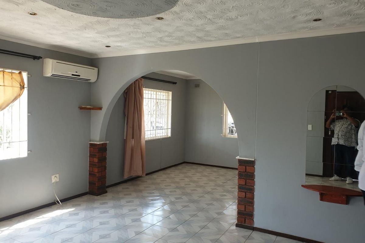 Spacious living area featuring a distinctive brick-accented archway, tiled flooring, and a wall-mounted air conditioning unit.