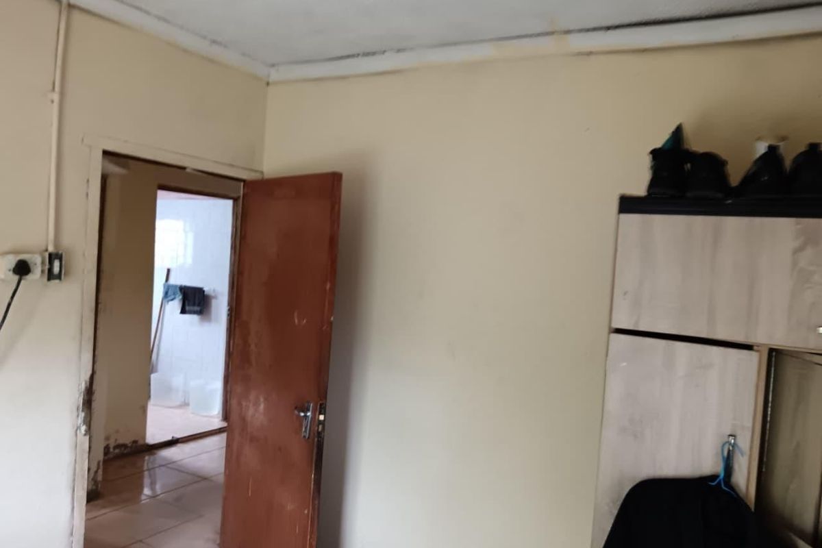 A bedroom interior featuring a built-in wardrobe and internal door, showing signs of wear including ceiling water staining and damaged wall finishes.