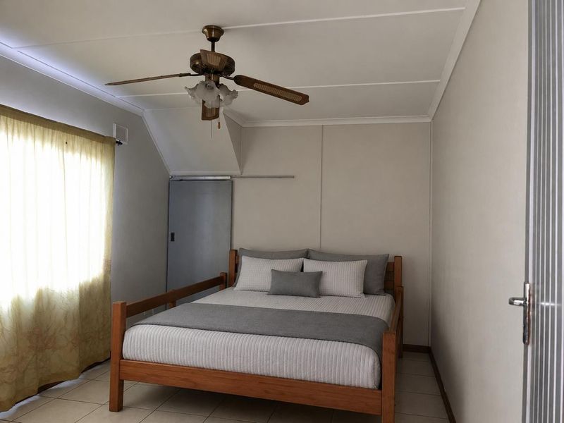 A functional bedroom featuring tiled flooring, a ceiling fan, and a sliding door, offering a neutral base for personalization.