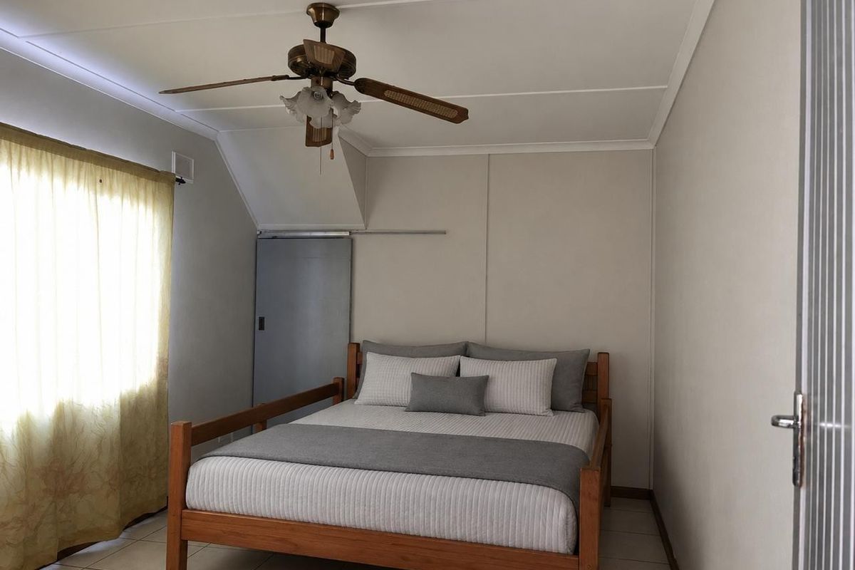 A functional bedroom featuring tiled flooring, a ceiling fan, and a sliding door, offering a neutral base for personalization.