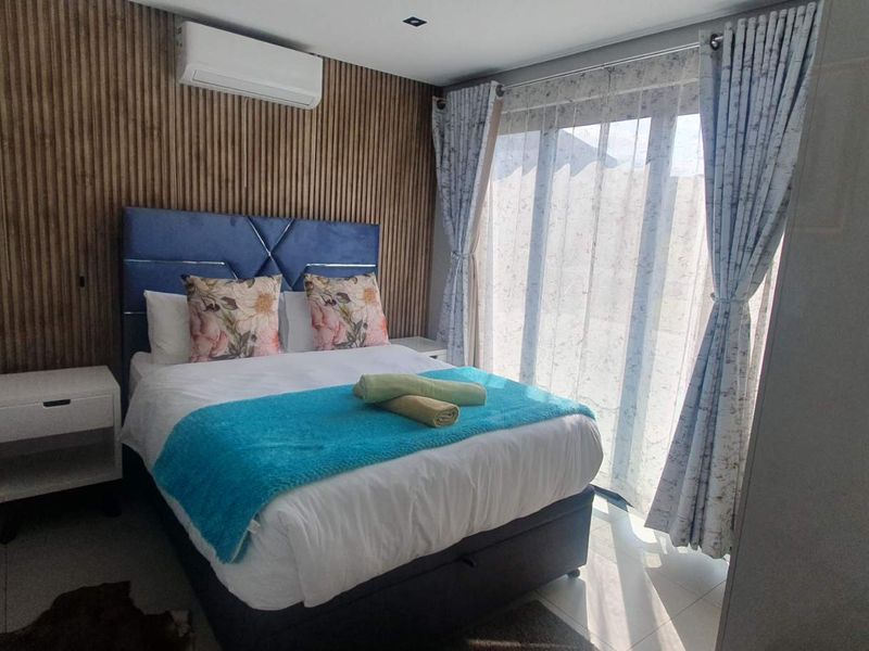 A modern bedroom featuring a timber slat accent wall, tiled flooring, and a sliding glass door providing natural light and access to the exterior.
