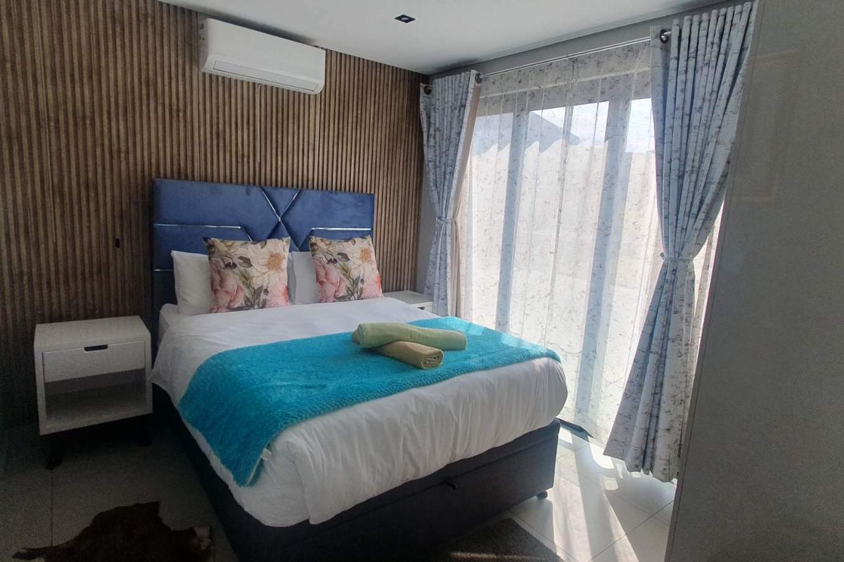 A modern bedroom featuring a timber slat accent wall, tiled flooring, and a sliding glass door providing natural light and access to the exterior.