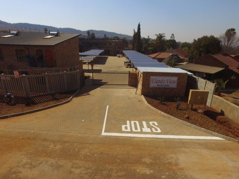 Aerial view of the apartment complex entrance, featuring a paved driveway, security gate, and covered parking bays.