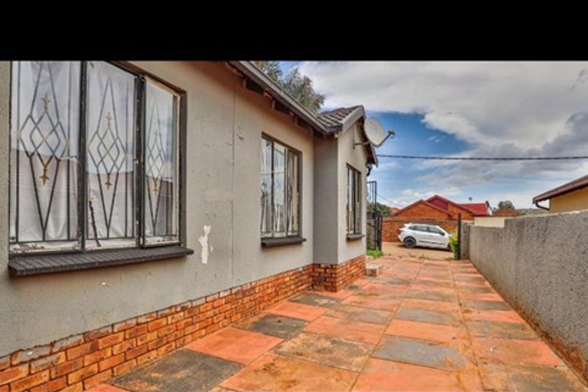 A side exterior view of the property featuring brick paving, boundary walls, and security bars on the windows.