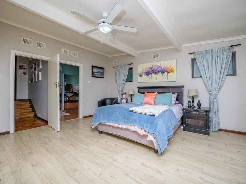 Spacious bedroom featuring light-toned laminate flooring, exposed ceiling beams, a central ceiling fan, and direct access to an en-suite bathroom.