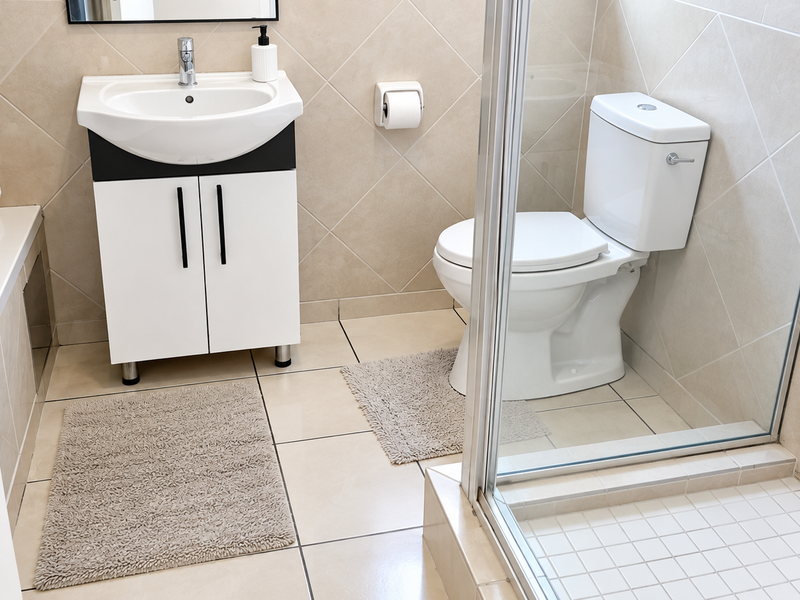 A clean, well-maintained bathroom featuring a modern vanity, a white toilet, and a glass-enclosed shower with neutral wall and floor tiling.