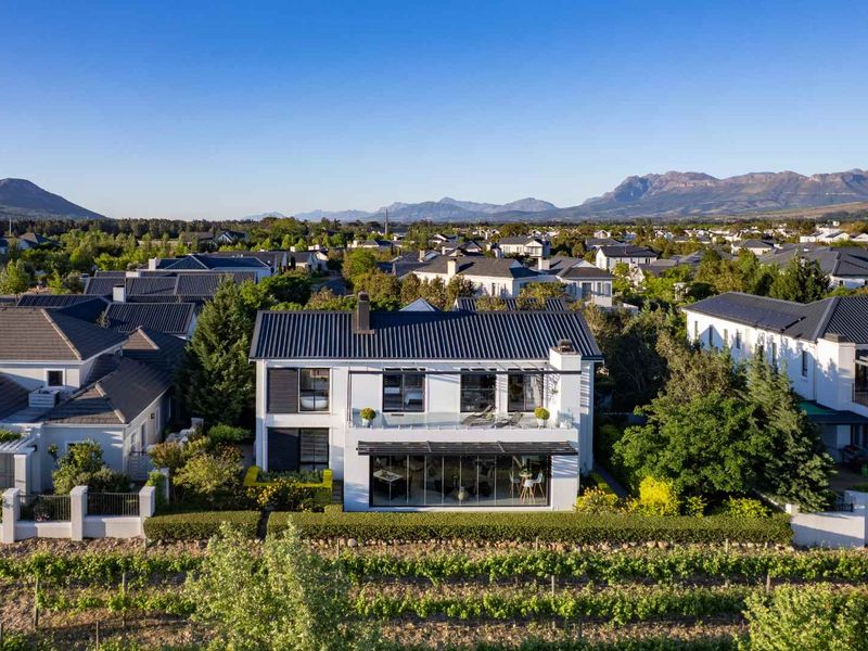 Aerial view of a modern two-story residential property featuring a metal roof, balcony with glass balustrade, and expansive ground-floor glass sliding doors.