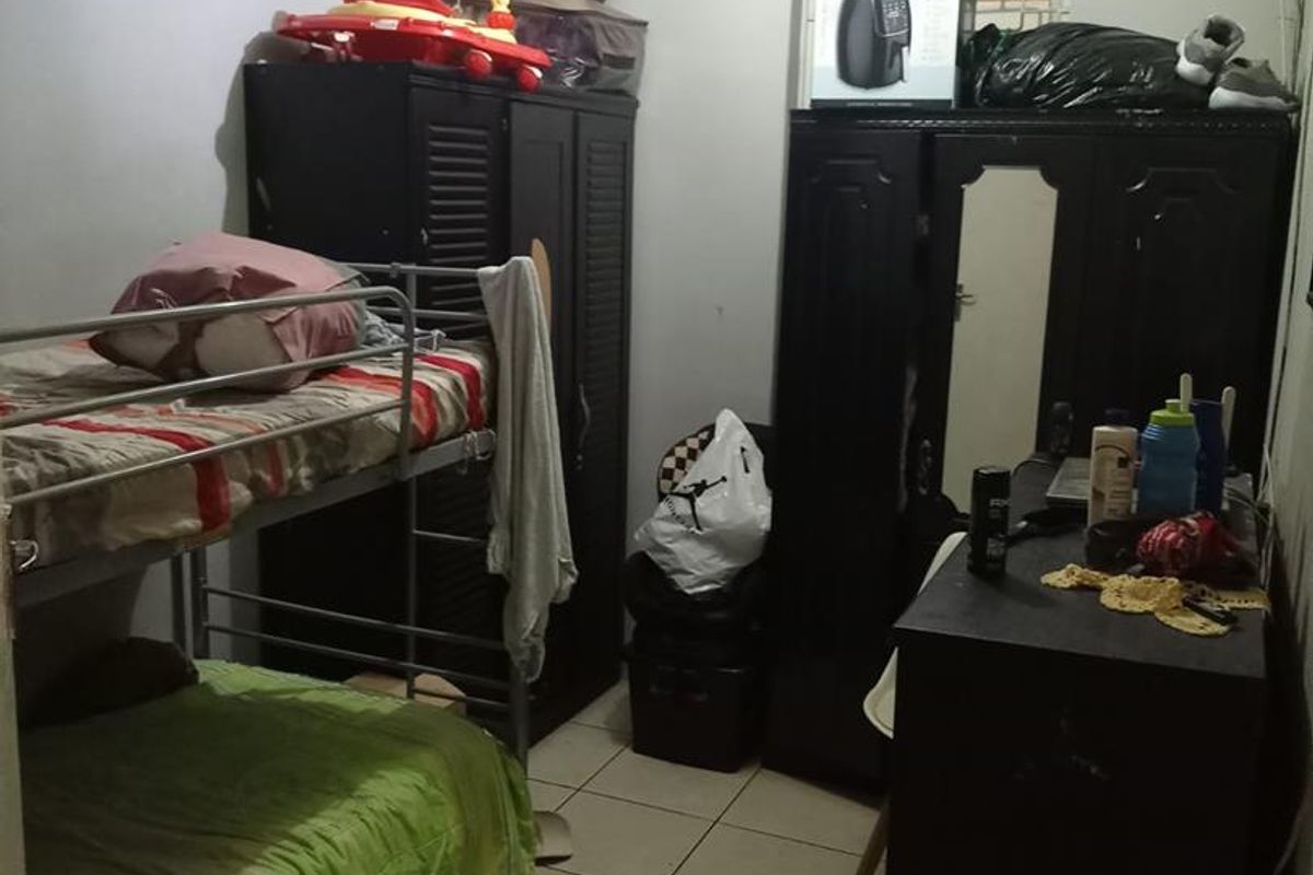 A compact bedroom featuring tiled flooring and basic finishes, currently utilized with multiple storage units and sleeping arrangements.